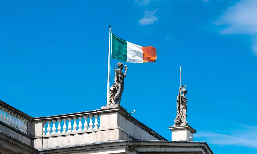 Bandeira da Irlanda hasteada sobre um edifício histórico em Dublin sob céu azul.