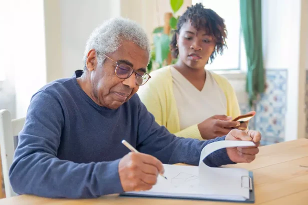 Homem idoso preenchendo documentos enquanto recebe apoio de uma cuidadora familiar em casa, ilustrando o contexto do Carer’s Allowance na Irlanda.
