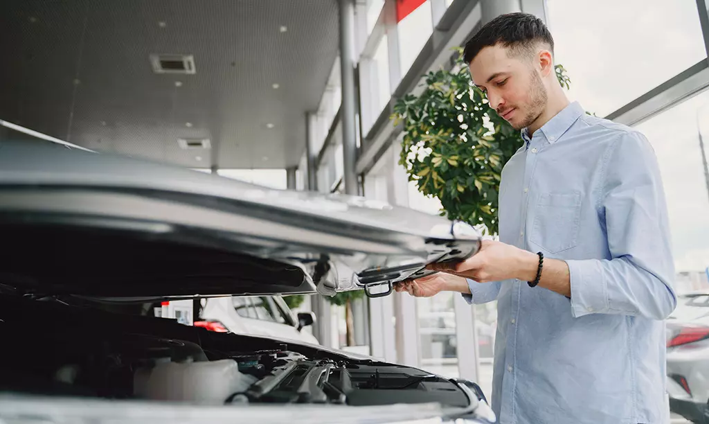 Pessoa inspecionando o motor de um carro antes da compra em uma concessionária na Irlanda.