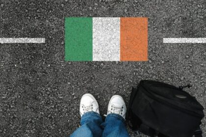 Pessoa com mala em frente à bandeira da Irlanda pintada no asfalto, representando imigração e mudança para o país.