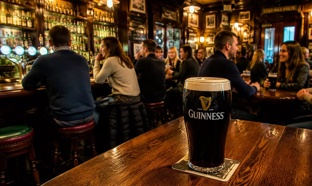 Pint de Guinness servido em um tradicional pub irlandês com clientes ao fundo.